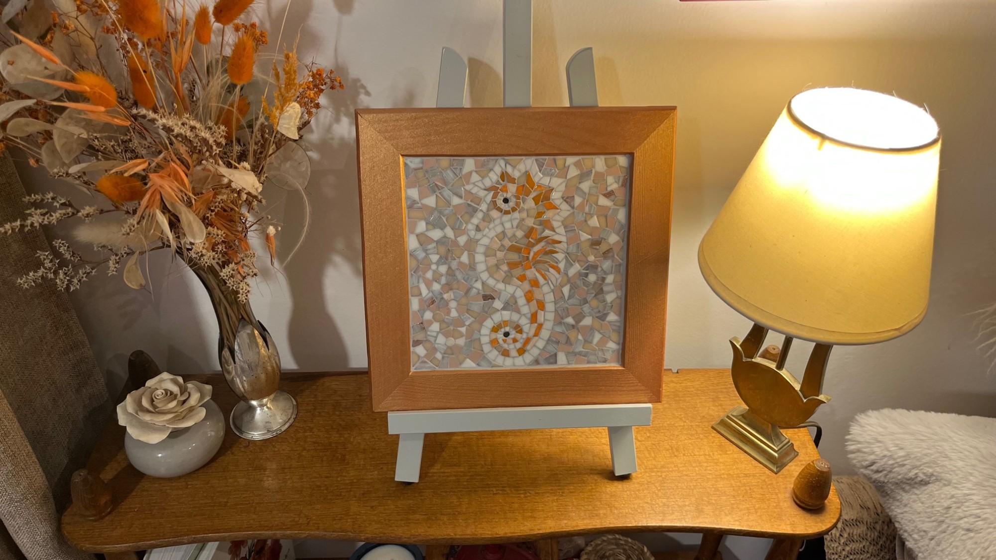 Tableau en mosaïque représentant un hippocampe orange et blanc encadré sur un chevalet en bois