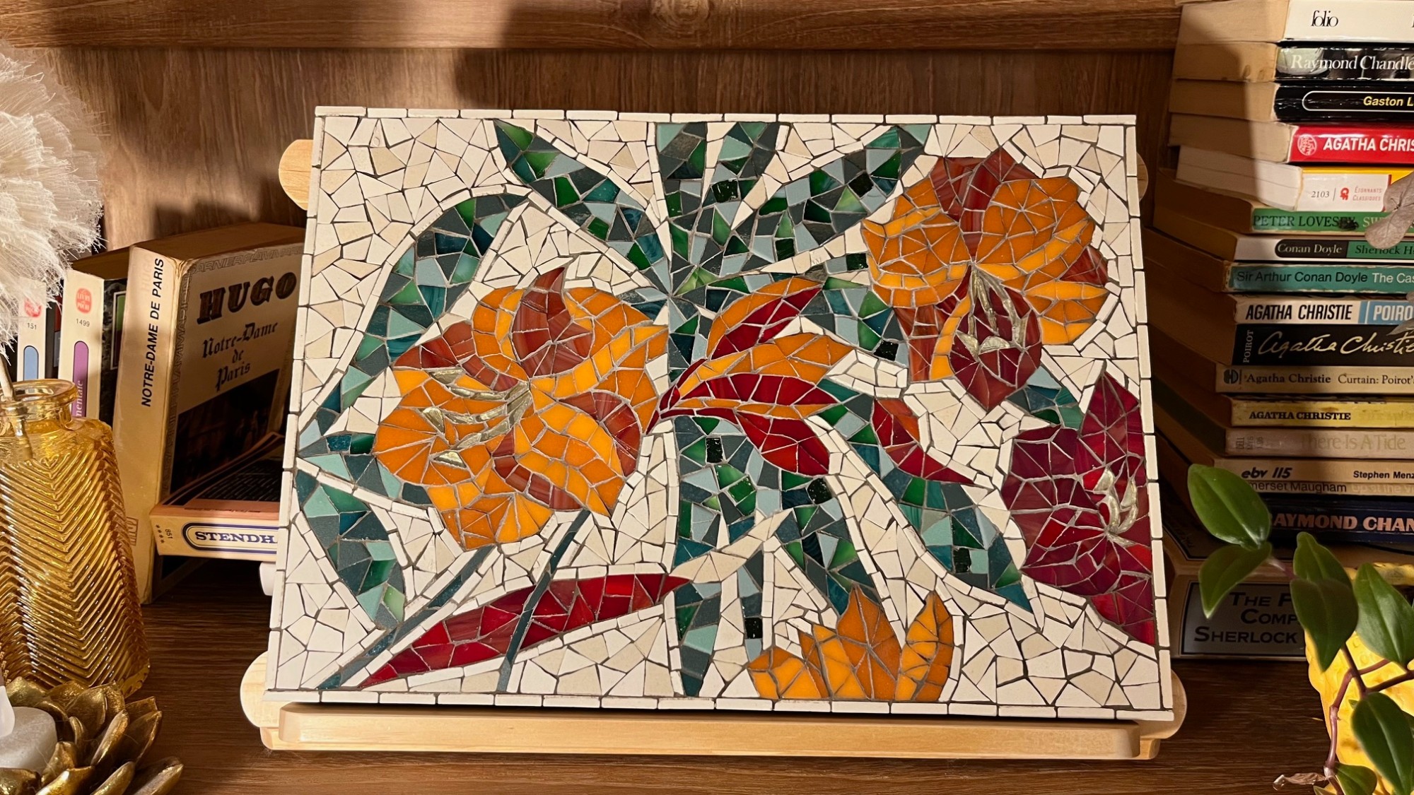 Tableau en mosaïque de fleurs stylisées orange et rouges posé sur une étagère