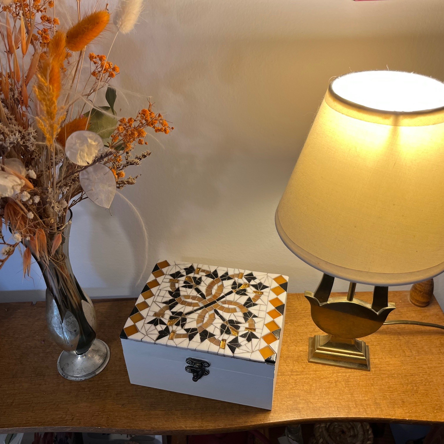 Boîte à bijoux artisanale décorée de mosaïque blanche, noire et dorée posée sur un meuble en bois